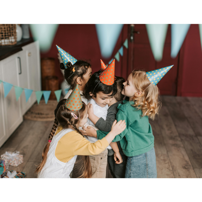 Children in party hats hugging at a joyful birthday celebration.