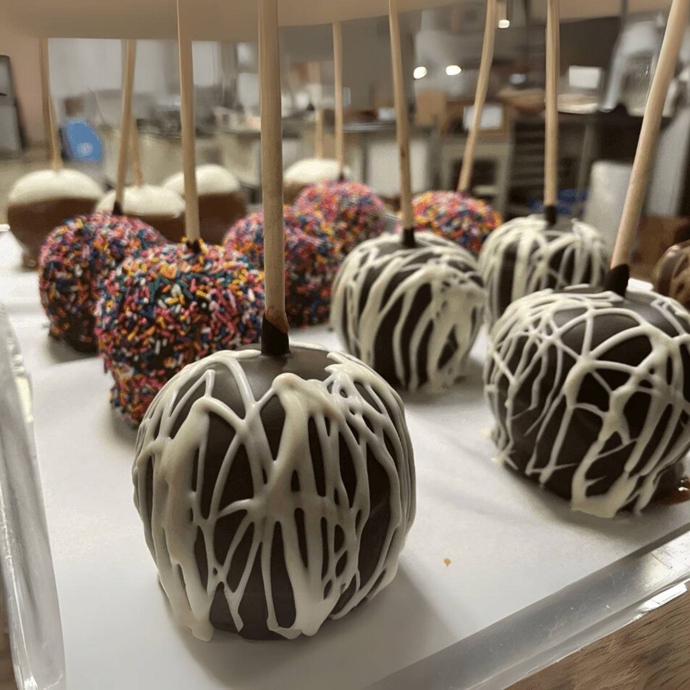 Decorative apples with white drizzle on sticks displayed on a tray.