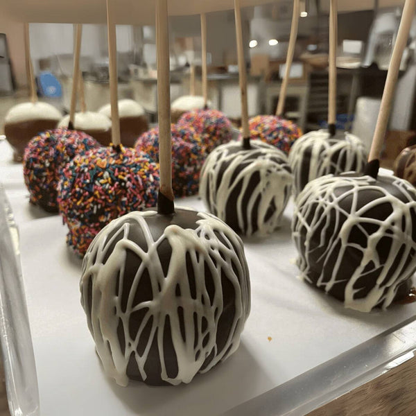 Decorative apples with white drizzle on sticks displayed on a tray.