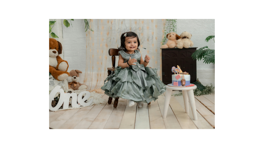 Smiling toddler girl in a fancy dress celebrating her first birthday with a themed cake and stuffed animals, illustrating age-specific birthday chocolate gift ideas for kids.