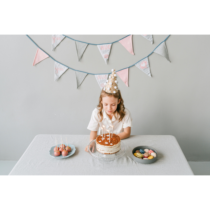 Young girl wearing a birthday hat about to blow out candles on a custom birthday cake, with personalized chocolate treats and macarons on the table, highlighting creative and personalized chocolate gift ideas for birthdays.