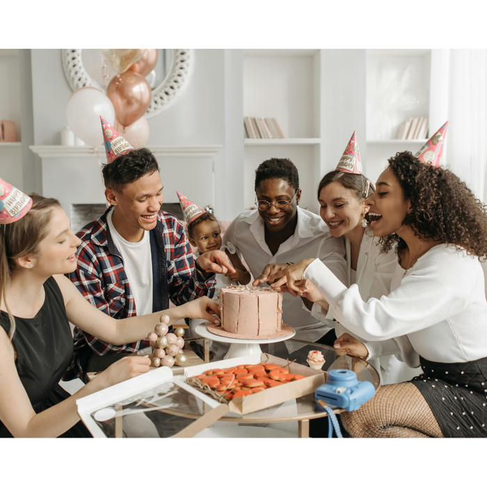 Diverse group of friends wearing party hats sharing cake and chocolates at a joyful birthday celebration, highlighting the importance of building birthday gift traditions that create lasting memories together