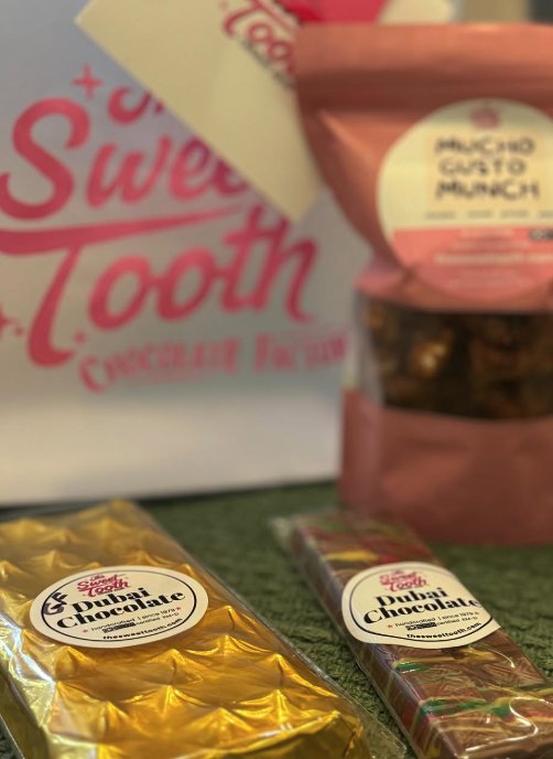 Two wrapped Dubai chocolate bars beside a snack pouch and a Sweet Tooth gift bag