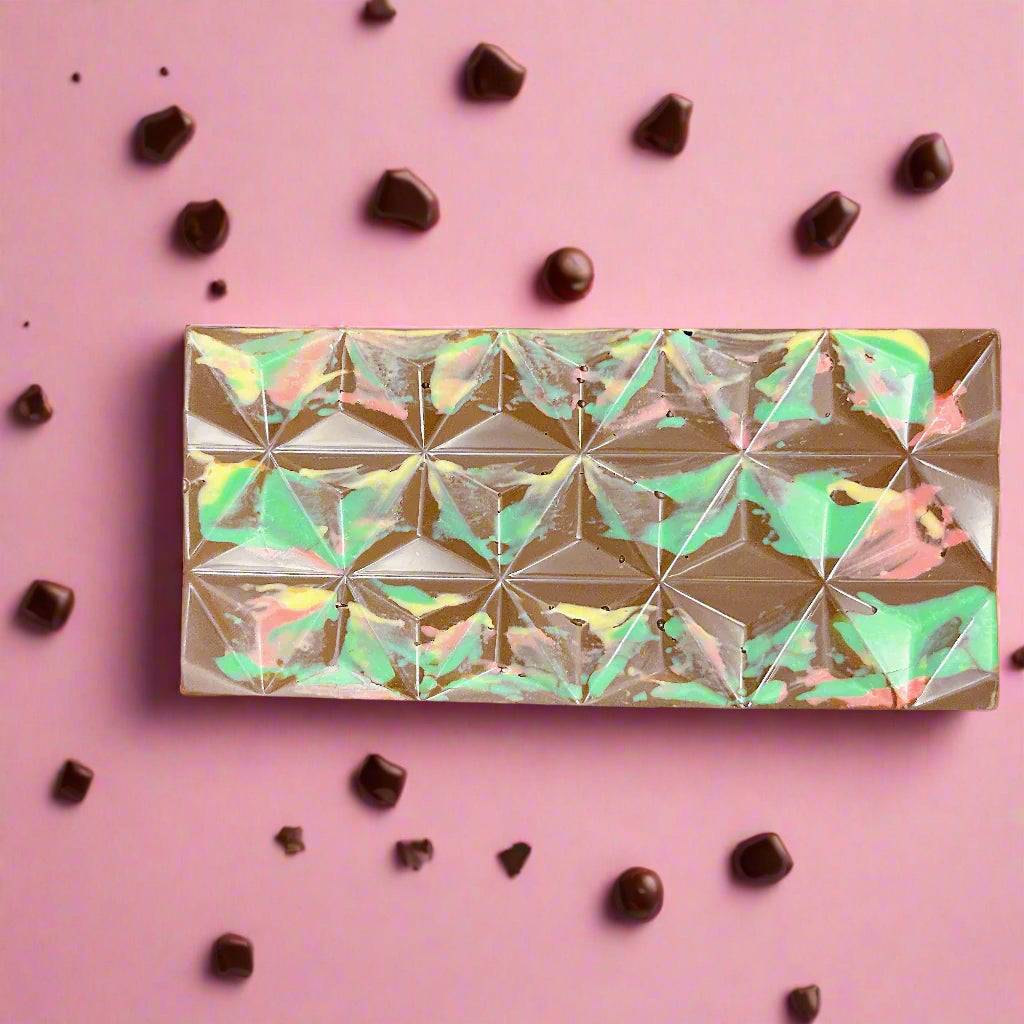Passover Dubai Chocolate Bar with colorful marbled design on geometric surface, surrounded by chocolate chunks on a pink background.