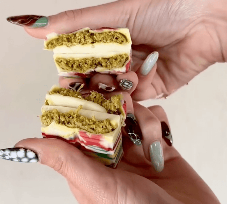 White chocolate Dubai Chocolate bar with colorful drizzle and pistachio filling, split in half to reveal layered texture.