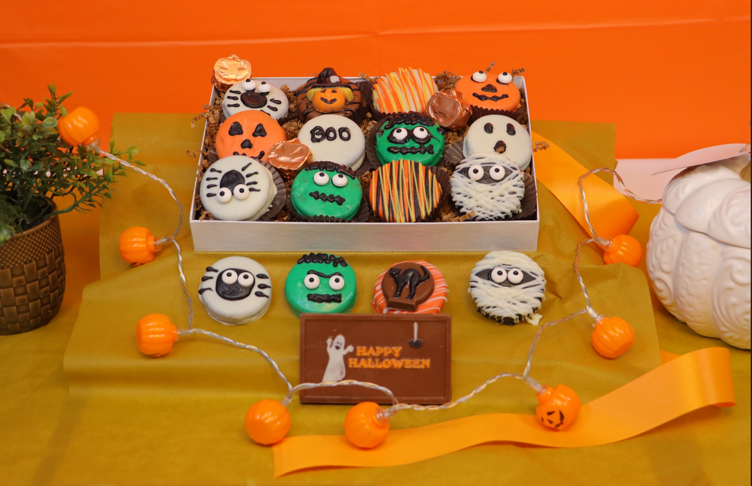 12-pack of Halloween-themed chocolate-dipped Oreos from The Sweet Tooth, featuring spooky designs like mummies, pumpkins, and monsters, beautifully arranged in a festive box