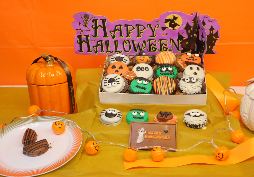 12-pack of Halloween-themed chocolate-dipped Oreos from The Sweet Tooth, featuring spooky designs like mummies, pumpkins, and monsters, beautifully arranged in a festive box