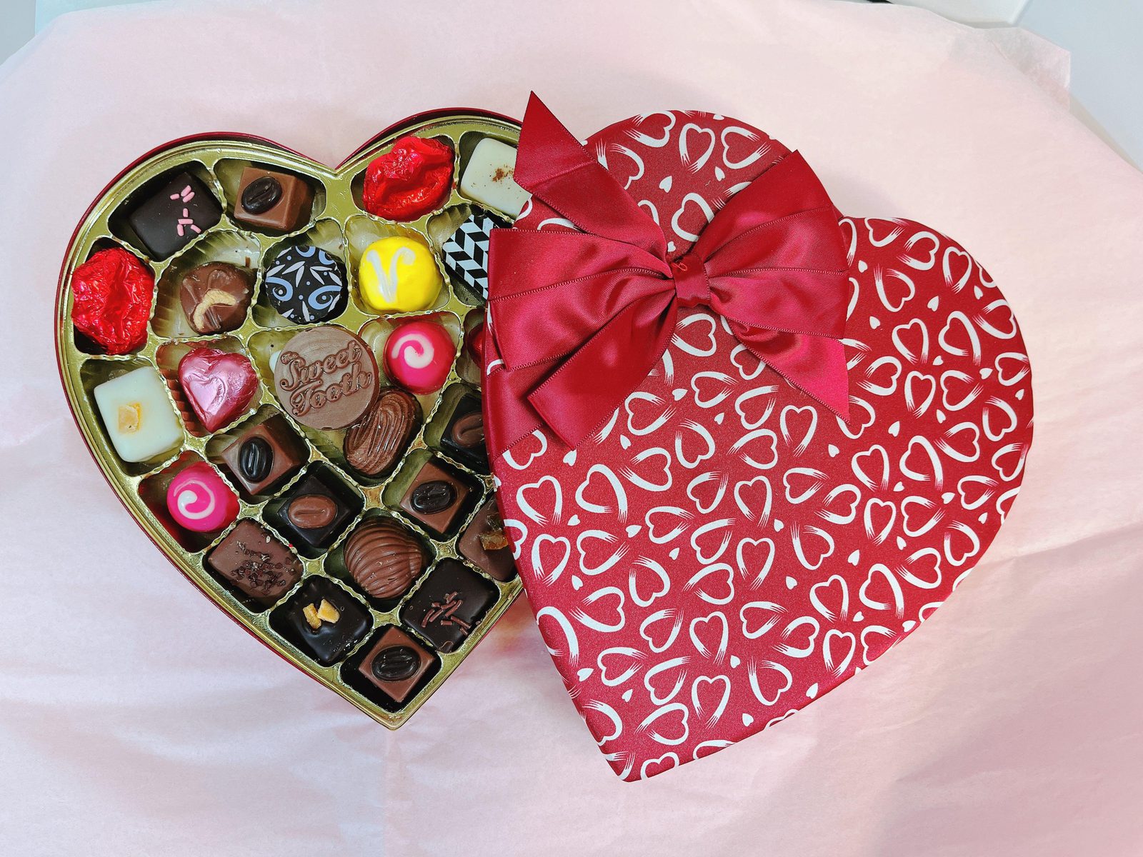 Open Heart-Shaped Box of Chocolates & Truffles with red heart-patterned lid and bow, showcasing premium chocolate-covered fruit selection.