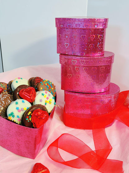 Stacked 3-tier heart-shaped gift boxes with glossy pink hearts design, showcasing elegant chocolate and truffle assortment beside them.