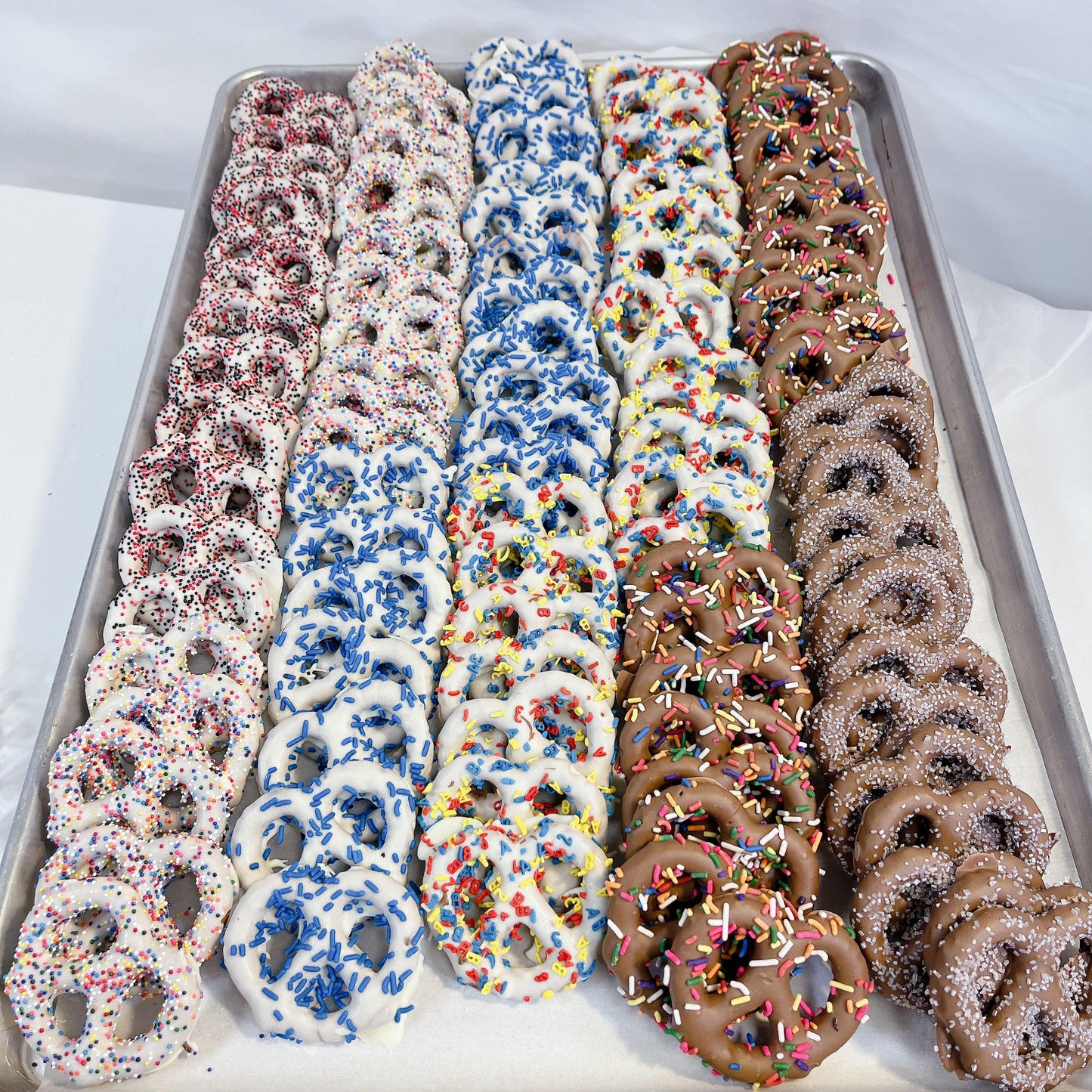 Chocolate Dipped Pretzels in assorted flavors with colorful sprinkles on a tray. Sweet and salty snack perfect for gifting or parties.