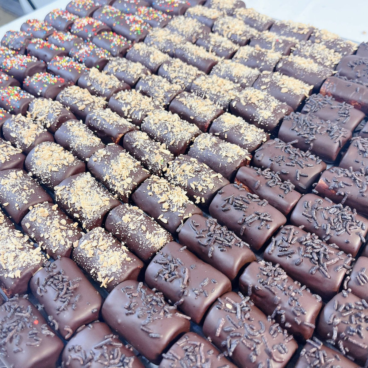 Rows of chocolate-covered logs with sprinkles from SUPREME - Passover, perfect for festive food gift assortments.