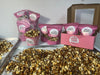Assorted Mucho Gusto Munch snack packs and tubs displayed with trays of chocolate-drizzled popcorn. Buy 1 Get 1 Free offer at The Sweet Tooth.