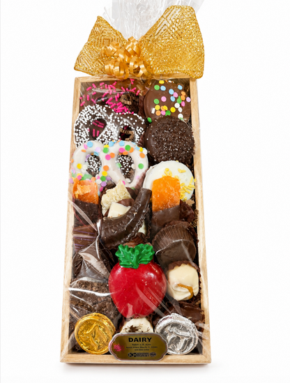 A wooden gift box filled with assorted chocolate treats, pretzels, trufles and a red apple-shaped candy, wrapped in clear cellophane and topped with a large gold bow for Rosh Hashana. 