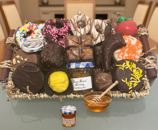 Assorted chocolate candies with decorative elements on a tray, accompanied by a small jar of jam and bowl of honey.