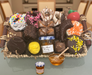 Assorted chocolate candies with decorative elements on a tray, accompanied by a small jar of jam and bowl of honey.