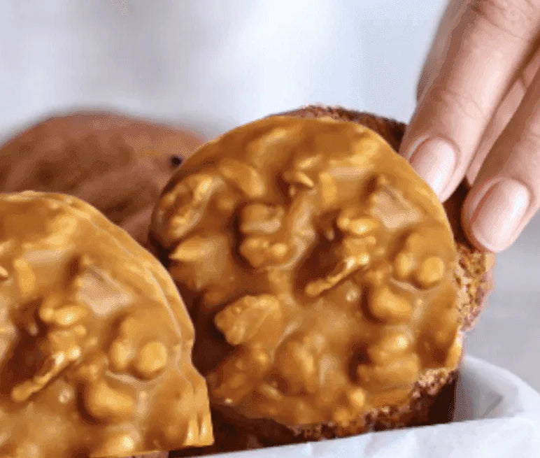 Hand holding a pecan praline with another one in the foreground on a white background