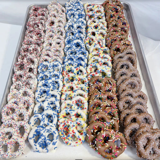 Assorted pretzels with different toppings on a baking sheet.