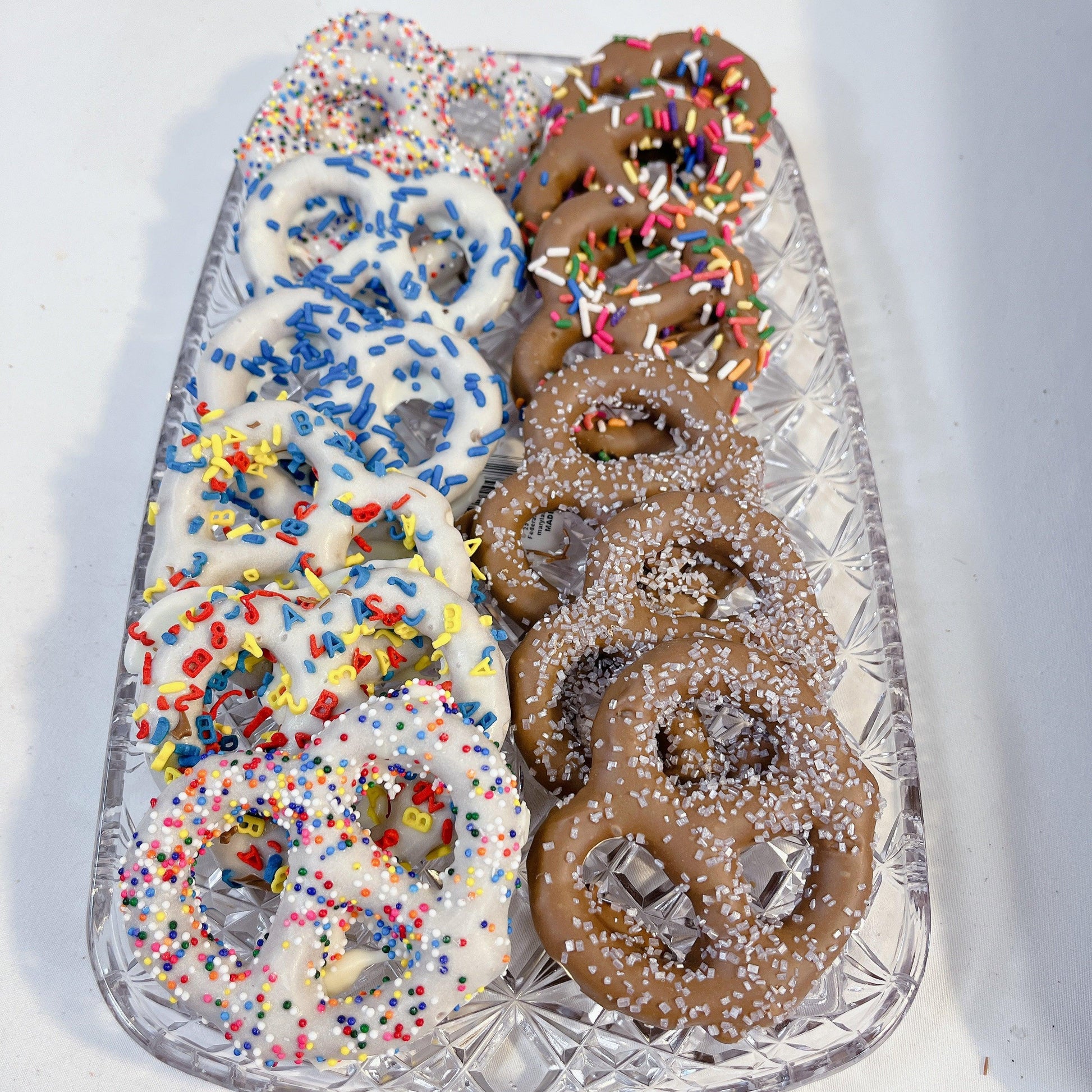 Gourmet Chocolate Dipped Pretzels with rainbow and letter sprinkles on a crystal tray. A crunchy sweet and salty treat for chocolate lovers.