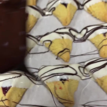 Freshly baked hamantaschen cookies dipped in white chocolate and drizzled with dark chocolate, cooling on a parchment-lined tray. Perfect for Purim celebrations.